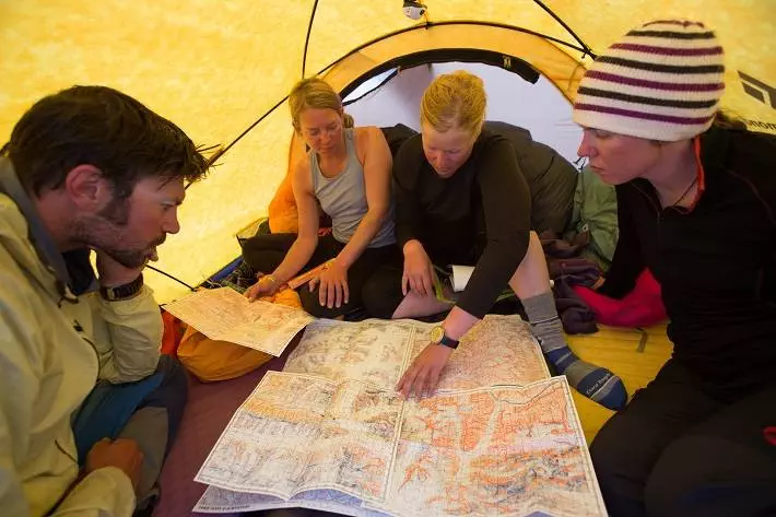 A group of adventure enthusiasts huddled in a tent, consulting a map for their skiing excursion.