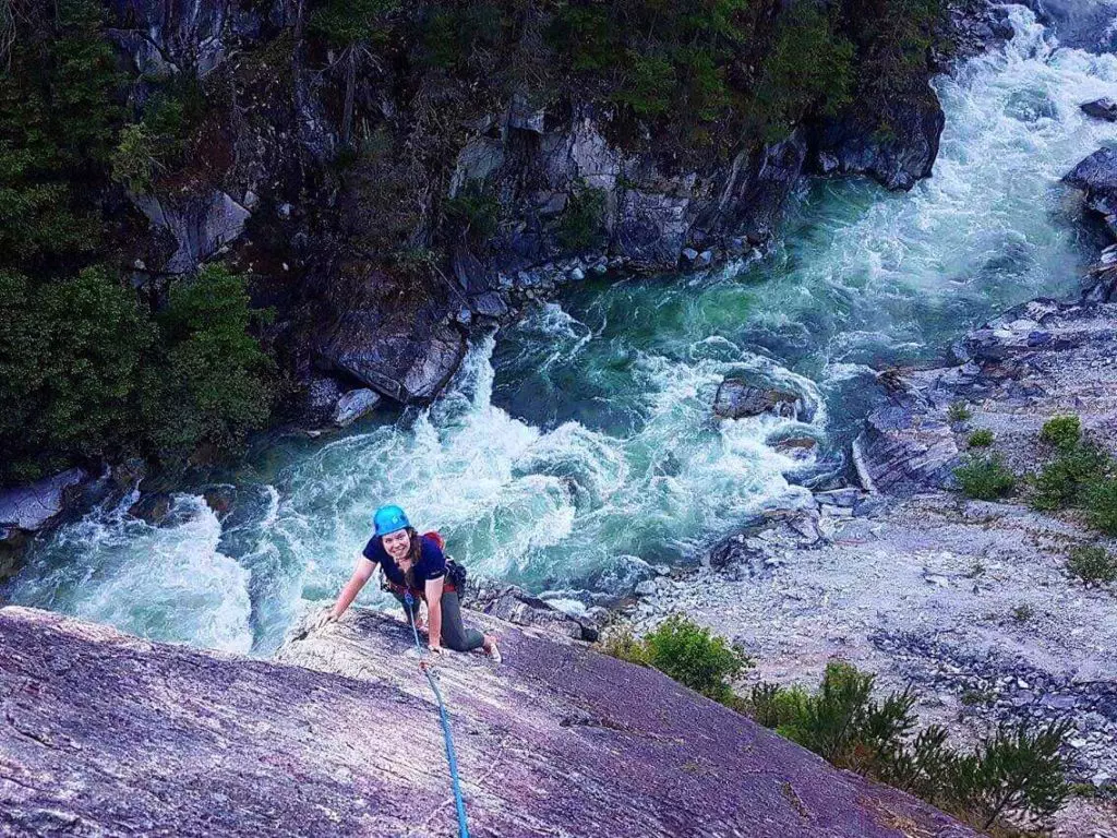 An adventurous rock climber scaling a cliff near a river.